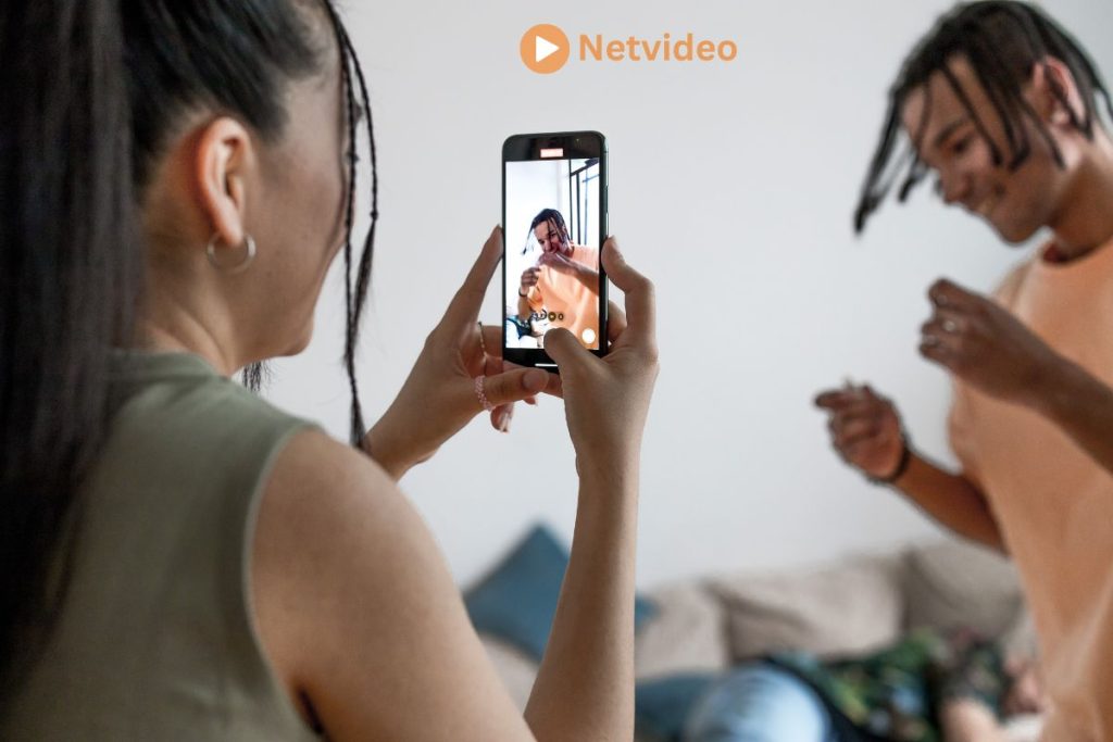 A woman records a man dancing using her smartphone, capturing a fun moment, with 'Netvideo' branding in the corner.